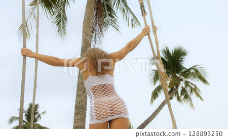Sexual woman spends her vacation at the seaside. The girl is swinging on a swing. 128893250