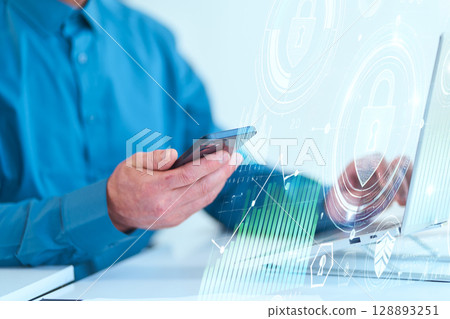 Businessman Using Smartphone And Laptop with Digital Security Icons in Modern Office Businessman Using Smartphone And Laptop with Digital Security Icons in Modern Office 128893251