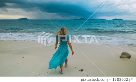 Charming woman with blonde curly long hair walk in beach, in stormy morning rain cloudy sea. Concept resort outdoor relax summer vacation, travel Charming woman with blonde curly long hair walk in beach, in stormy morning rain cloudy sea. Concept resort outdoor relax summer vacation, travel 128893254