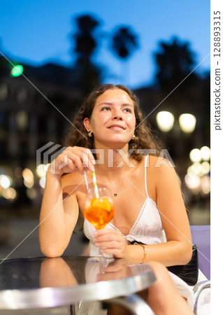 On summer outside of cafe, girl is relaxing at table, drinking chilled coctail. 128893315