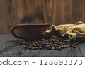 Rustic cup and burlap sack with roasted coffee beans on wooden surface 128893373