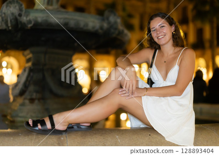 young woman sitting near a fountain in the evening young woman sitting near a fountain in the evening 128893404
