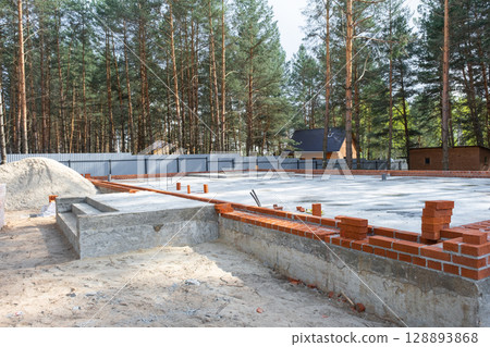 Concrete slab of foundation of house with laid pipes start of construction on project. Construction of cottages, design, engineering communications. Concrete slab of foundation of house with laid pipes start of construction on project. Construction of cottages, design, engineering communications. 128893868