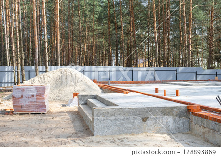 Concrete slab of foundation of house with laid pipes start of construction on project. Construction of cottages, design, engineering communications. Concrete slab of foundation of house with laid pipes start of construction on project. Construction of cottages, design, engineering communications. 128893869