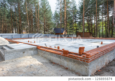 Concrete slab of foundation of house with laid pipes start of construction on project. Construction of cottages, design, engineering communications. 128893874