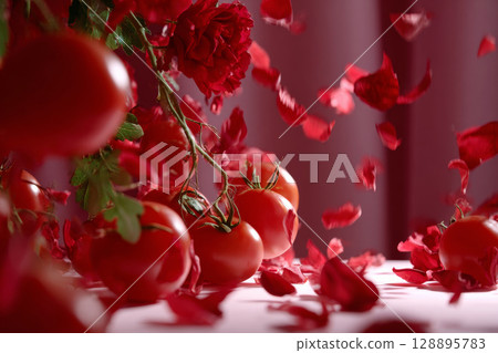 Surreal composition of tomatoes and roses with falling petals in dreamy red setting 128895783