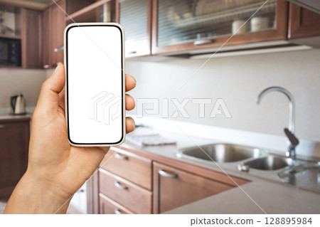 Smart home control in kitchen by apps in smartphone. Man hand holding mobile phone with white blank screen for design. 128895984