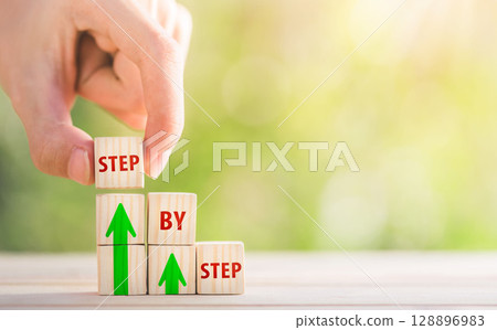 The word step by step on wooden cubes. Achievement or progress in business career. The word step by step on wooden cubes. Achievement or progress in business career. 128896983