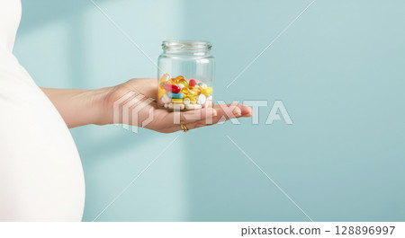 Pregnant woman holding a jar of colorful pills. Prenatal vitamins, maternal health, and healthy pregnancy. 128896997