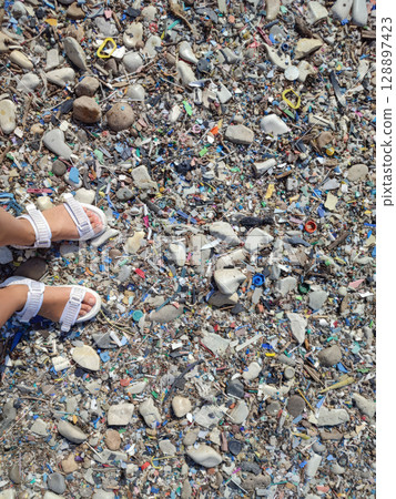 A person is standing on a beach with trash all around them. A person is standing on a beach with trash all around them. 128897423
