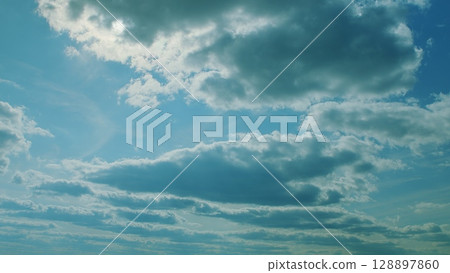 A Beautiful Blue Sky with Fluffy White Clouds and Bright Radiant Sunlight Shining Down 128897860