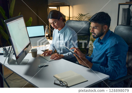 Two Professionals Working on Computer and Tablet in Modern Office Environment 128898079