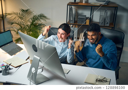 Excited Office Colleagues Celebrating Success Together at Workplace in Front of Computer 128898100