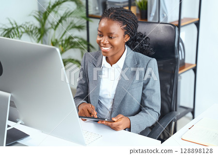 Professional Woman Smiling and Working at a Desk in a Modern Office Setting Professional Woman Smiling and Working at a Desk in a Modern Office Setting 128898128