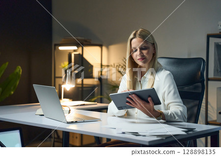 Young Professional Woman Working Late Night With Tablet at Modern Office Desk 128898135