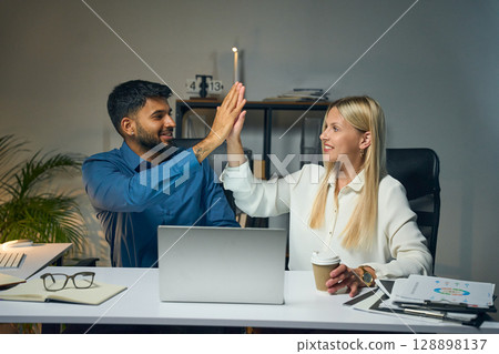 Two Colleagues Celebrate Success With High Five While Working Together in Office 128898137