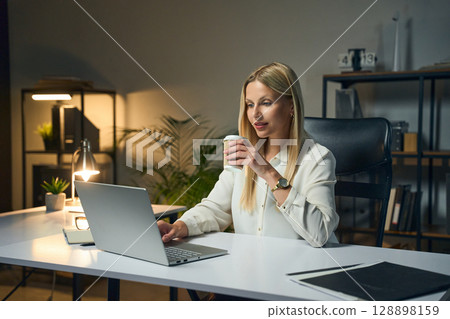 Professional Woman Working on Laptop in Modern Office with a Cup of Coffee Professional Woman Working on Laptop in Modern Office with a Cup of Coffee 128898159