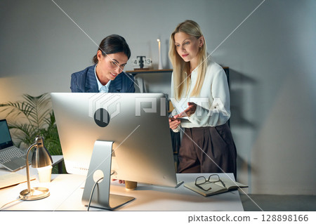 Two Businesswomen Collaborating In Office While Analyzing Data on Computer Screen 128898166