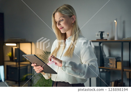 Professional Woman Using a Tablet in a Modern Office Setting at Night 128898194