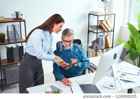 Colleagues Collaborating in a Modern Office with Digital Devices and Graphs 128898205