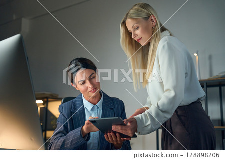 Two Professional Women Collaborating on a Digital Tablet in Office Environment 128898206