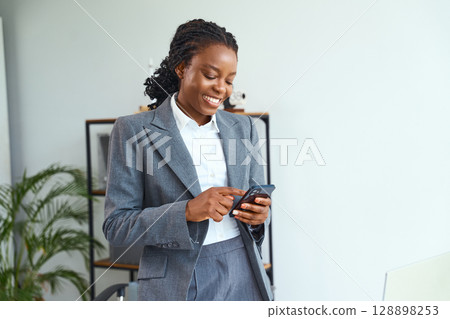 Smiling Professional Woman Using Smartphone in Modern Office Setting 128898253