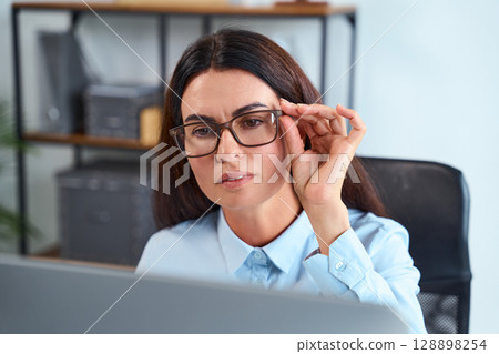 Focused Businesswoman Adjusting Glasses And Working On A Computer In Office 128898254