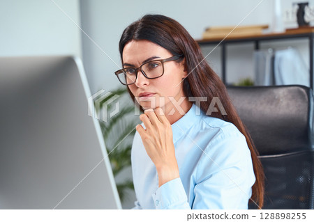 Focused Business Woman Working at Desk in Modern Office Environment 128898255
