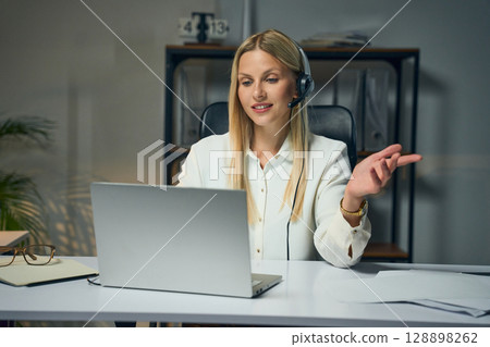 Professional Businesswoman Conducting Online Meeting With Headset and Laptop in Office Professional Businesswoman Conducting Online Meeting With Headset and Laptop in Office 128898262