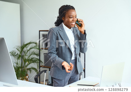 Businesswoman In Professional Attire Talking Cheerfully On Phone In Office Environment Businesswoman In Professional Attire Talking Cheerfully On Phone In Office Environment 128898279