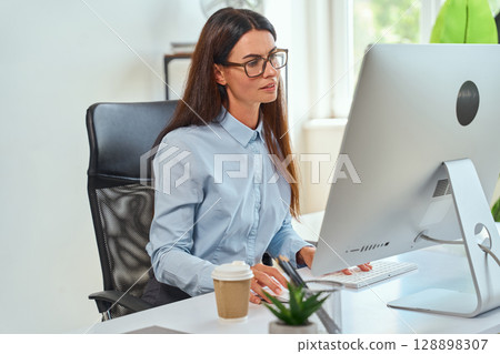 Professional Woman Working on Computer Desk in Well-Lit Office Setting 128898307