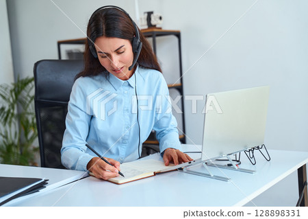 Professional Woman Working From Home Office With Headset And Laptop Writing Notes 128898331
