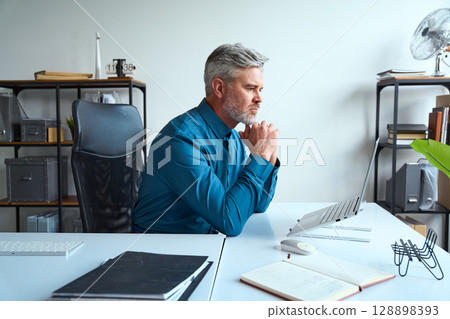 Professional Man Focused on Work at Desk in Modern Office Environment Professional Man Focused on Work at Desk in Modern Office Environment 128898393