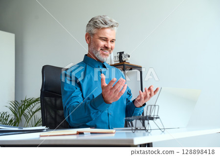 Mature Businessman Conducting A Virtual Meeting While Smiling In Office Environment 128898418