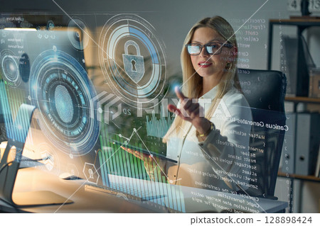 Modern Businesswoman Analyzing Cybersecurity Data on Interactive Holographic Screen in Office 128898424
