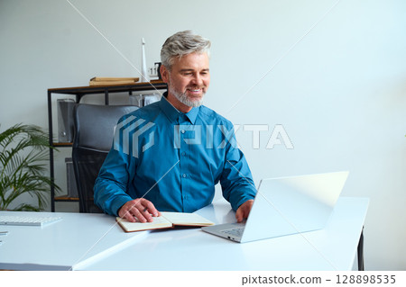 Smiling Professional Man Working on Laptop at Desk in Bright Modern Office 128898535