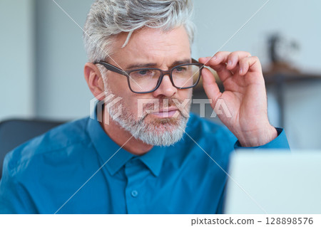 Focused Senior Professional Wearing Glasses Working on a Computer in a Modern Office 128898576