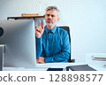 Confident Mature Businessman Thinking While Working at His Desk in a Modern Office 128898577