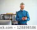 Smiling Mature Businessman Checking His Smartphone in a Modern Office Environment 128898586