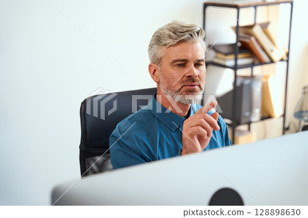 Professional Man Using Computer In Office With Focused Expression And Modern Attire 128898630