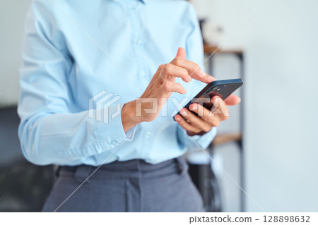 Professional Businesswoman Using Smartphone Indoors While Dressed in Formal Office Attire 128898632