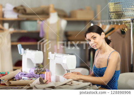 Woman seamstress sews on sewing machine in workshop 128898906