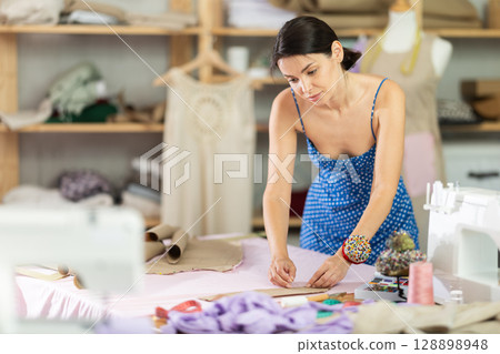 Young female seamstress attaching template to fabric Young female seamstress attaching template to fabric 128898948