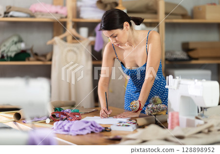 Young woman seamstress draws sketch on paper 128898952