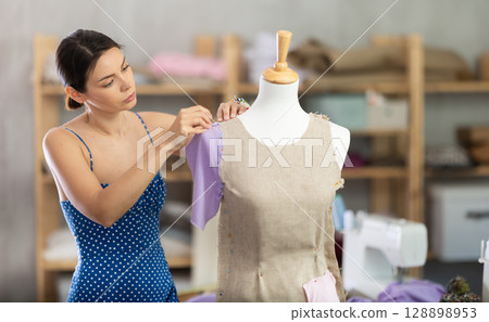 Woman seamstress adjusts clothes on mannequin Woman seamstress adjusts clothes on mannequin 128898953