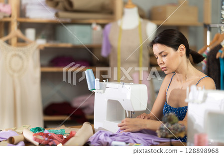 Woman seamstress sews on sewing machine in workshop 128898968