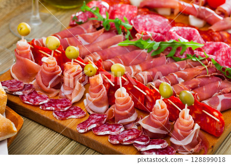 Slicing sausages fuet, ham, salami, chorizo with cherry tomatoes and olives 128899018