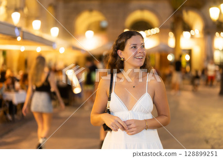 young woman walks along an evening street in Barcelona 128899251