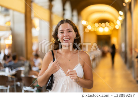 In evening, young smiling girl walks along city street Placa Real In evening, young smiling girl walks along city street Placa Real 128899287