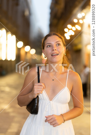Young woman walking along a lit street with a cafe Young woman walking along a lit street with a cafe 128899320
